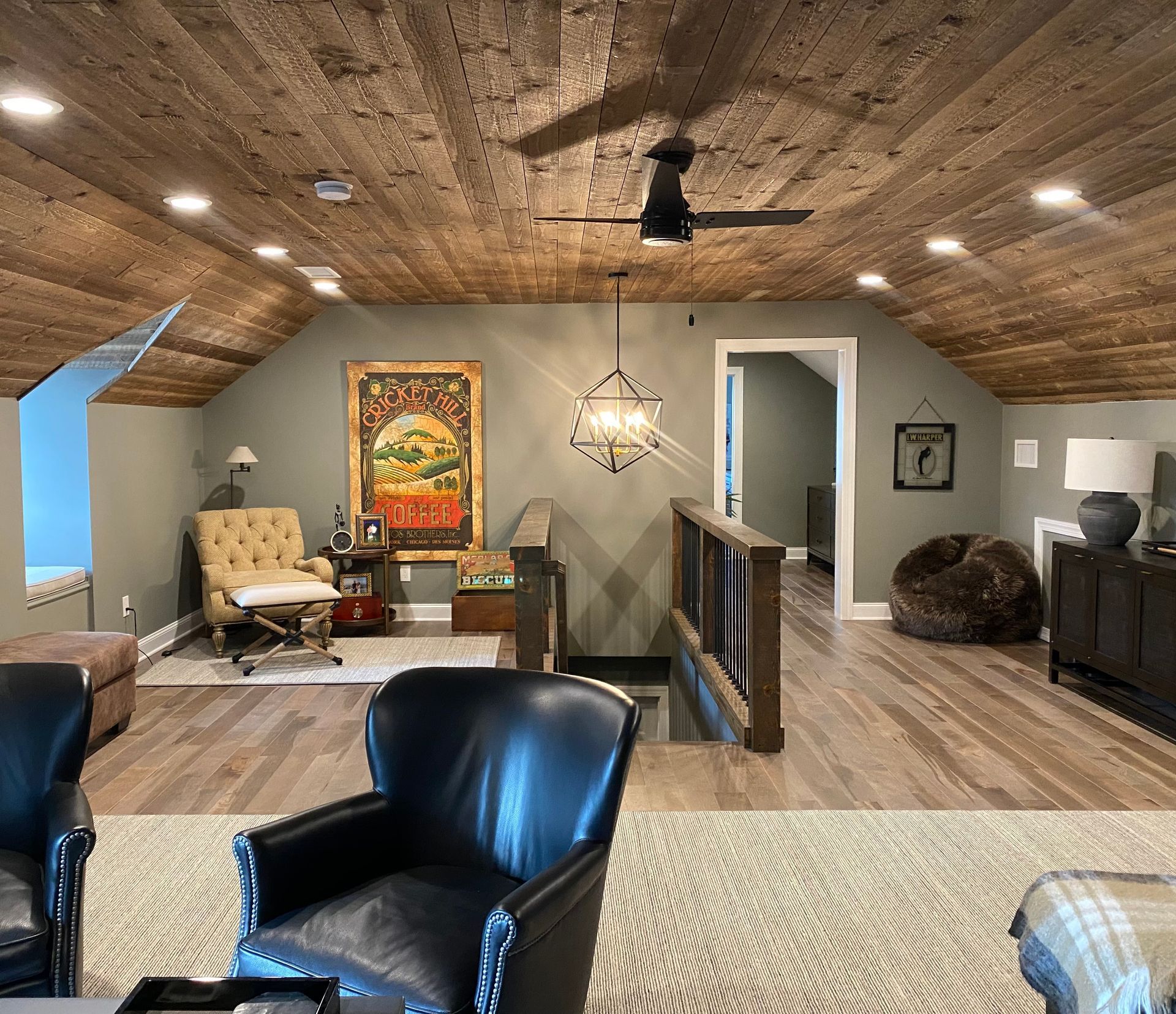 Loft living room with wood ceiling, black chairs, patterned rug, chandelier, and colorful wall art.