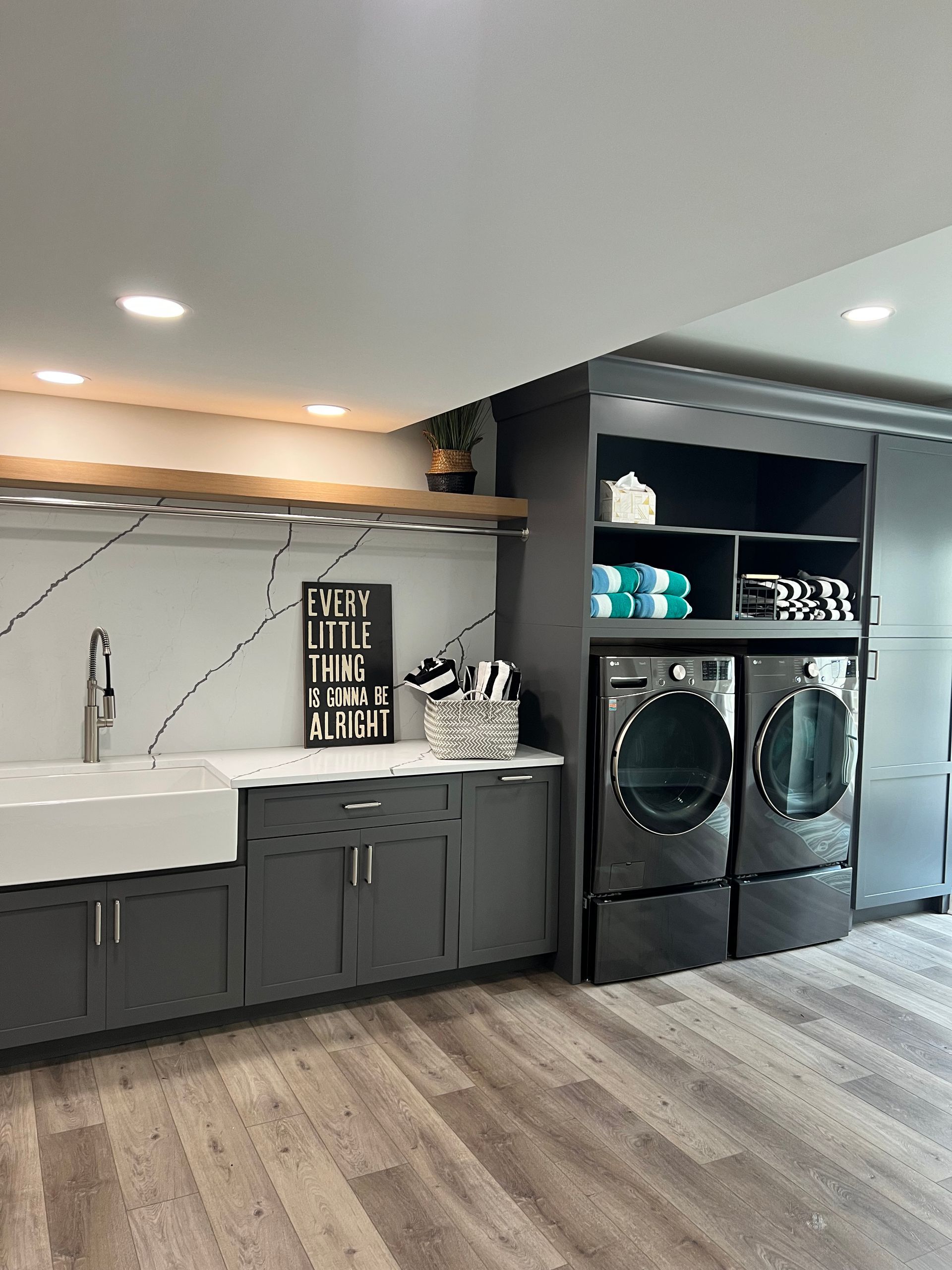 Modern laundry room with gray cabinets, white sink, black washer and dryer, and wood-look flooring