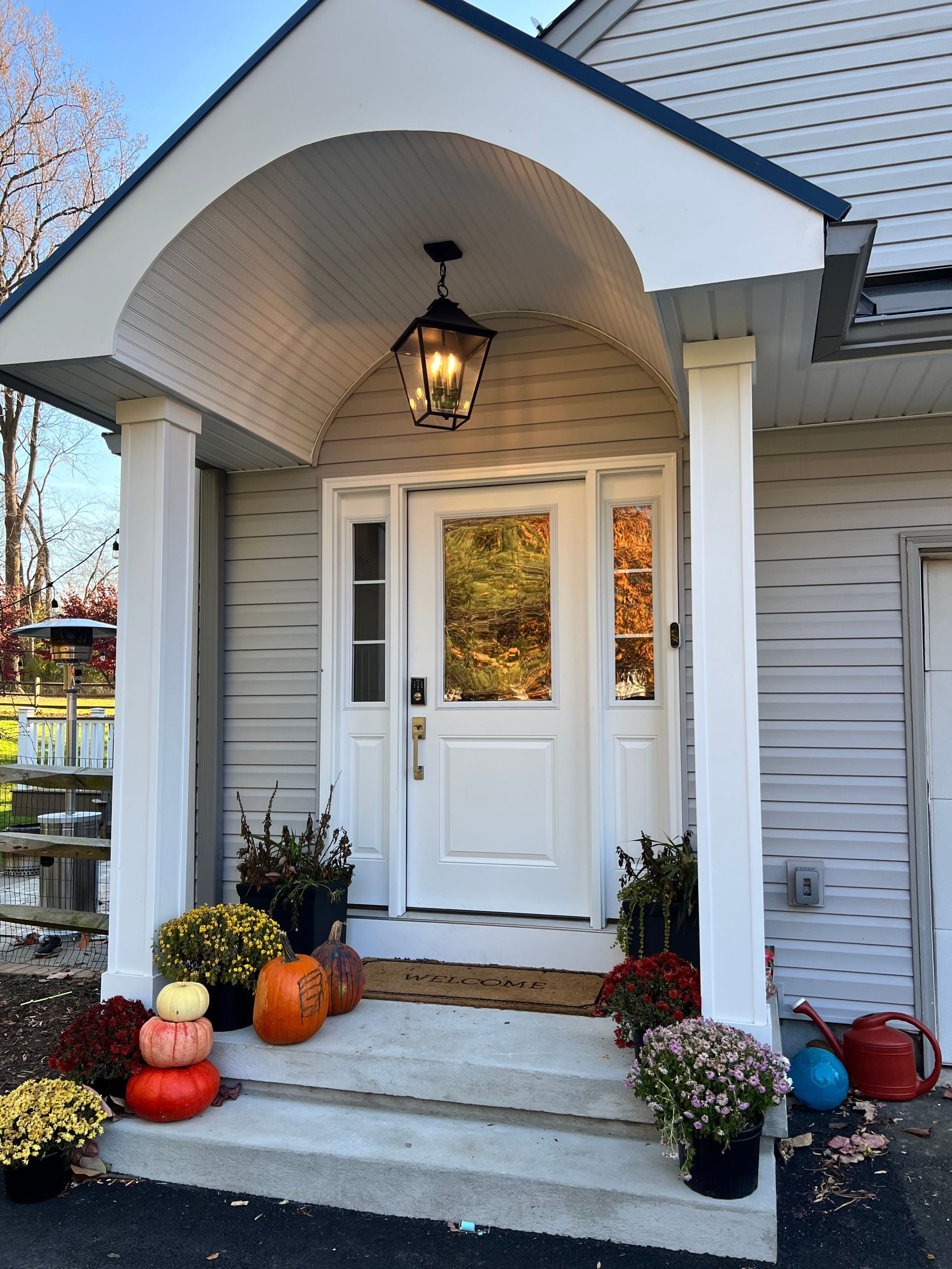 Front porch with white arched entry, hanging lantern, and fall pumpkins and mums by the steps