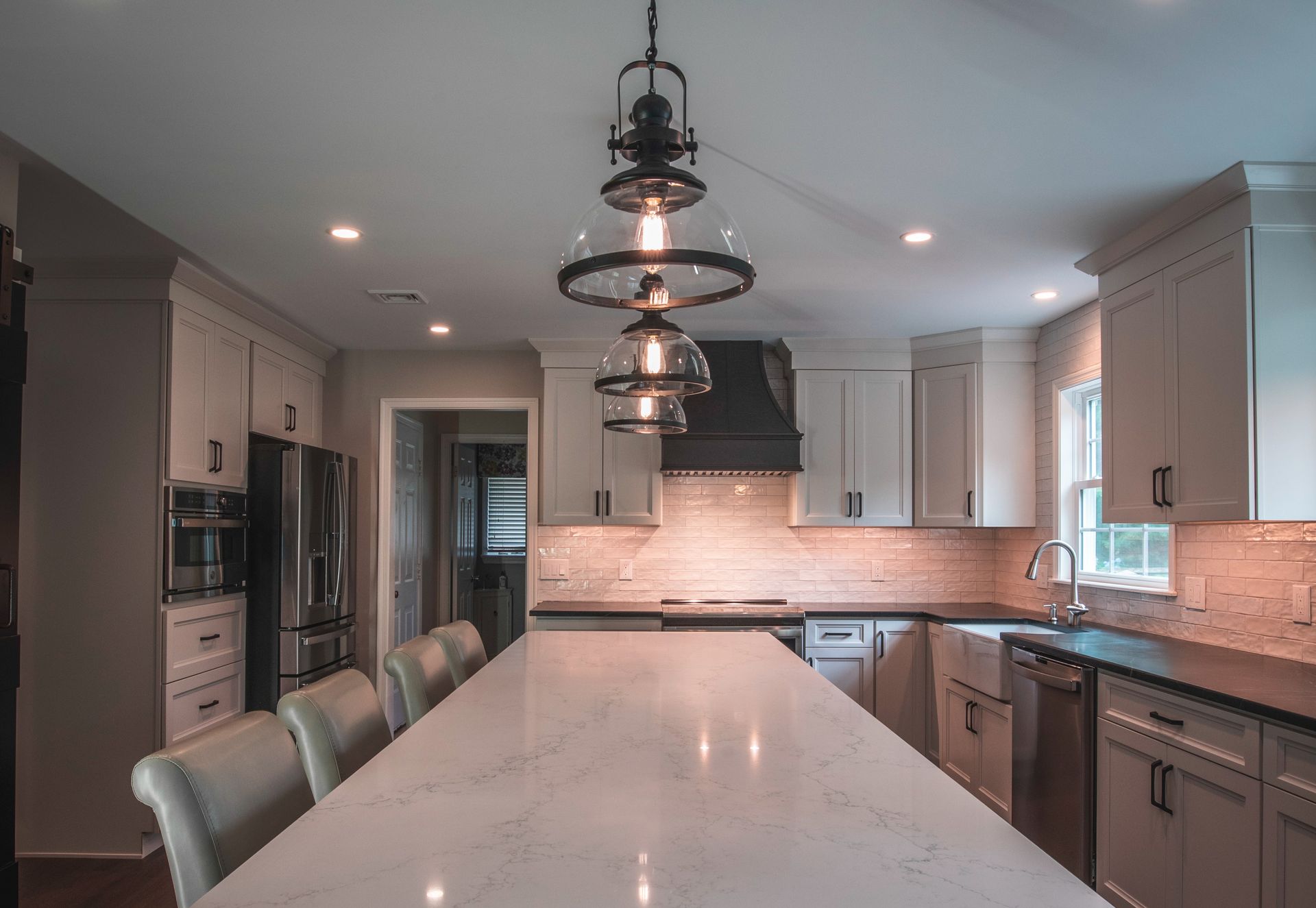 Modern kitchen with large white island, pendant lights, gray cabinets, and stainless appliances