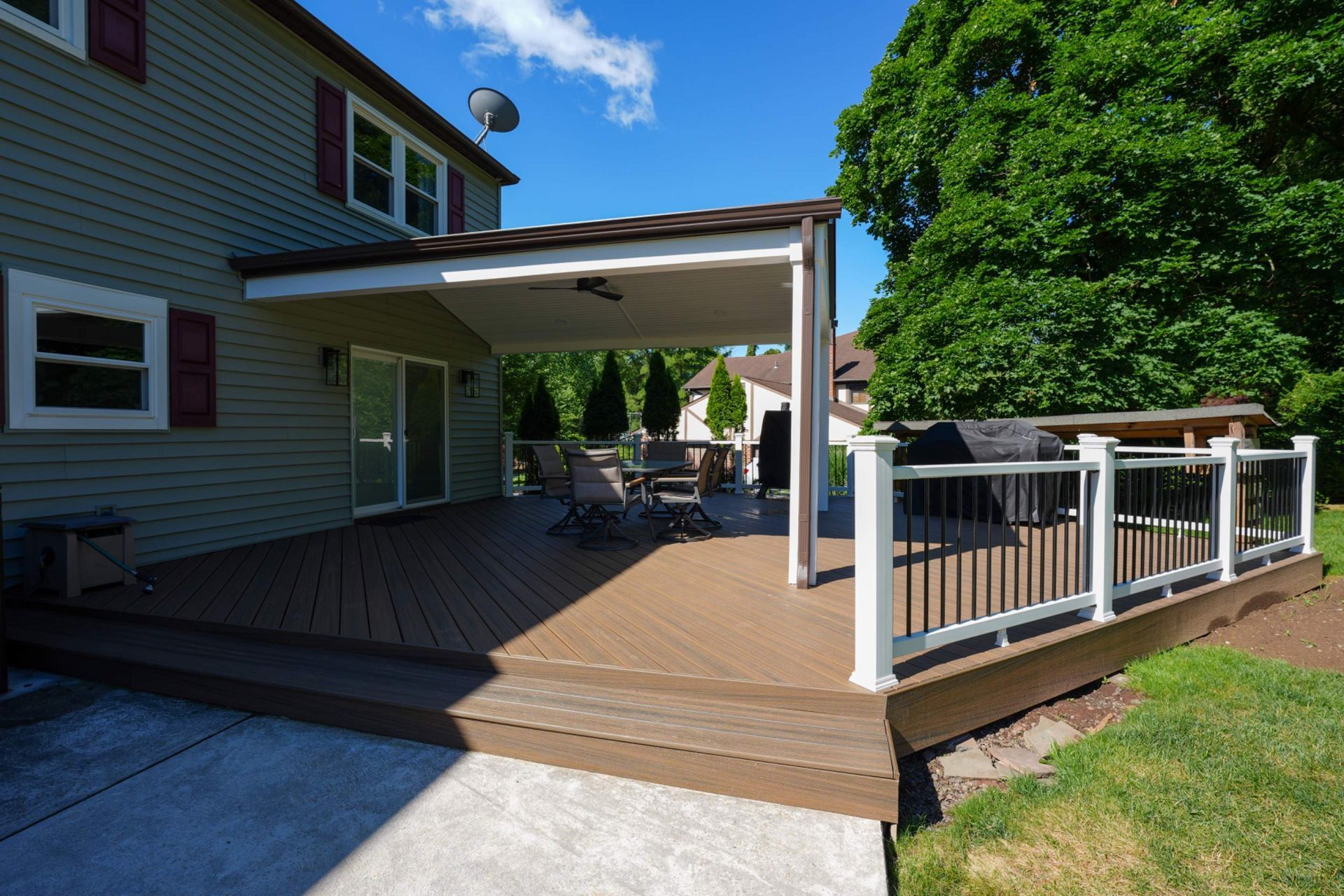Backyard deck with covered patio, wooden railing, and house exterior on a sunny day