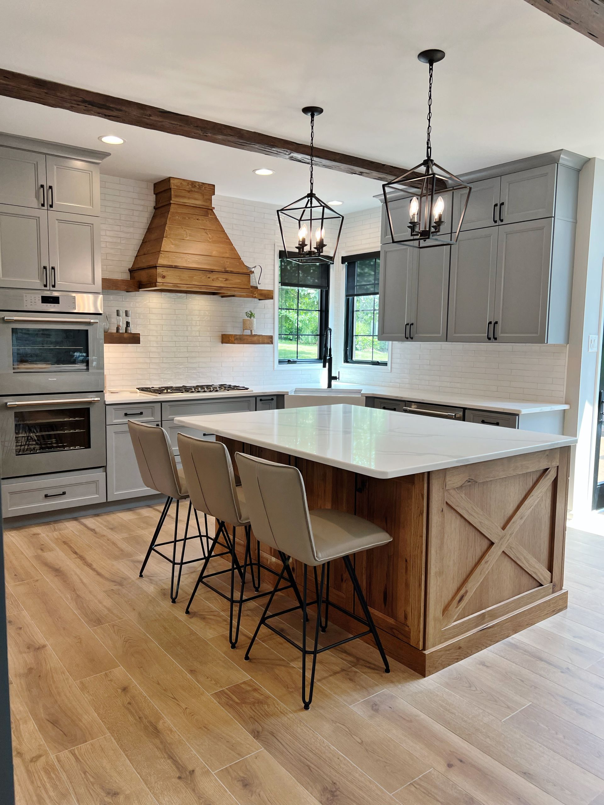 Bright modern kitchen with island, bar stools, gray cabinets, and woven range hood