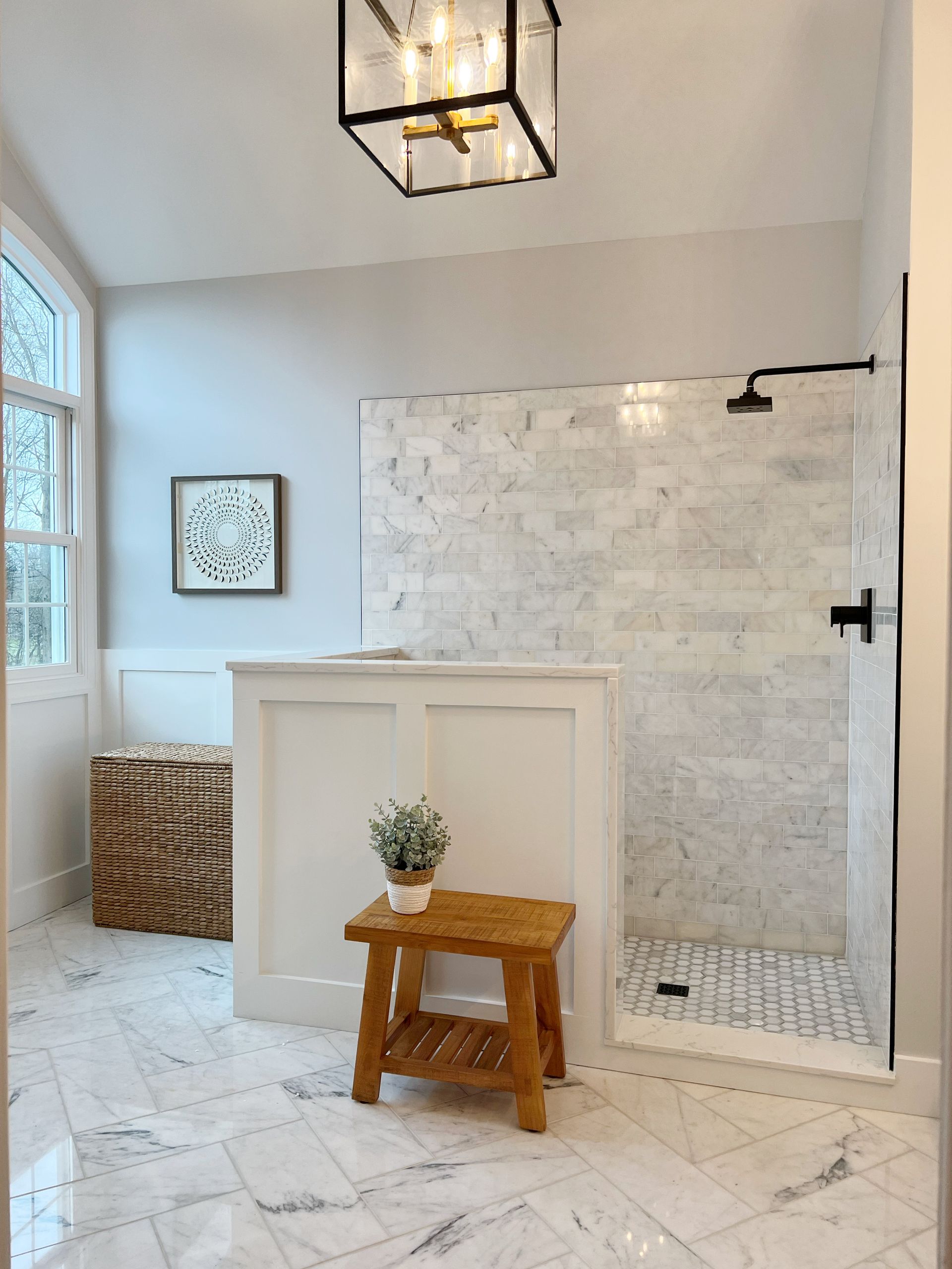 Bright bathroom with white tile, walk-in shower, vanity, and a small wooden step stool with a plant.