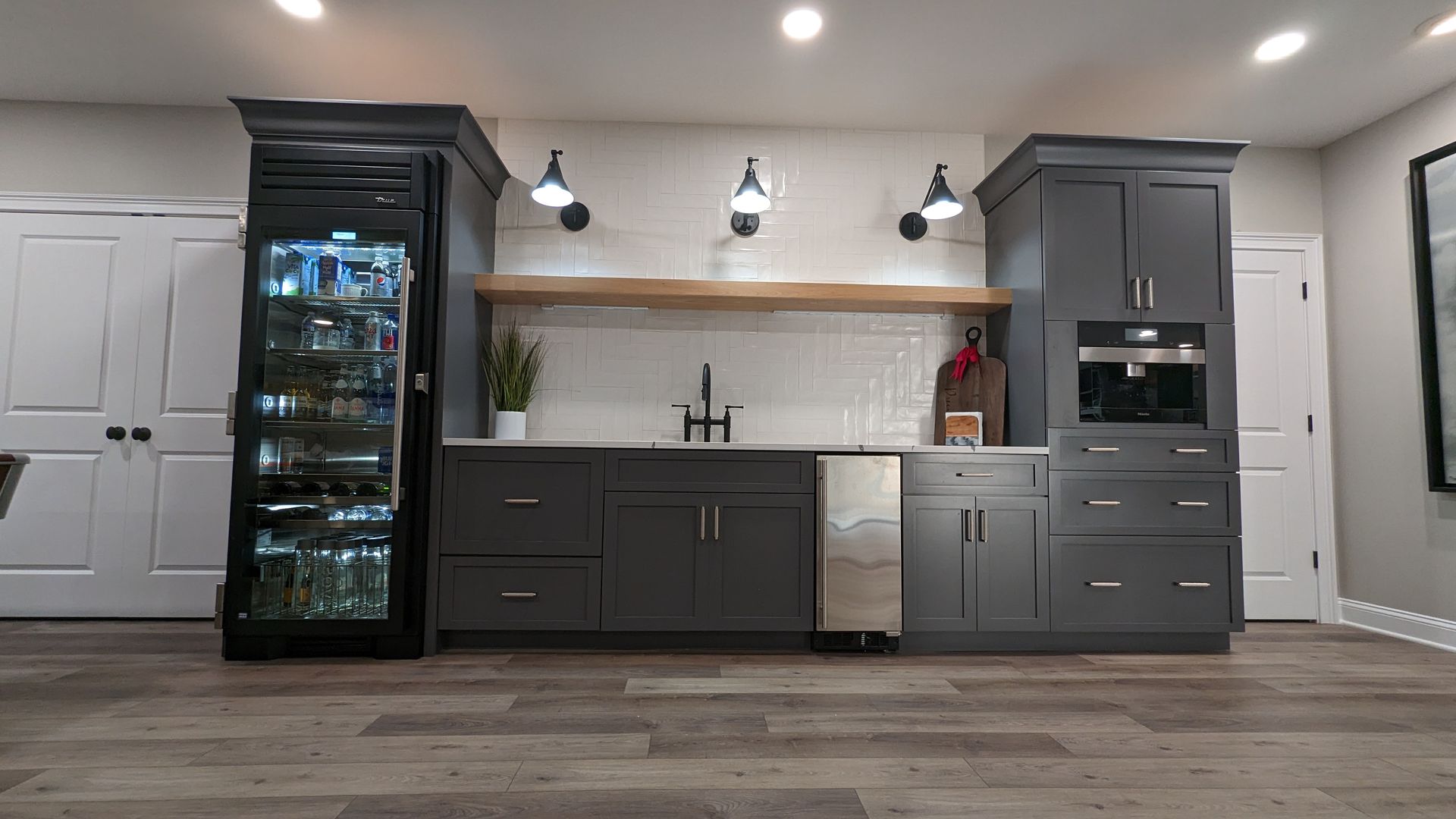Modern kitchen with dark cabinets, wine fridge, light wood floor, and white countertops under pendant lights