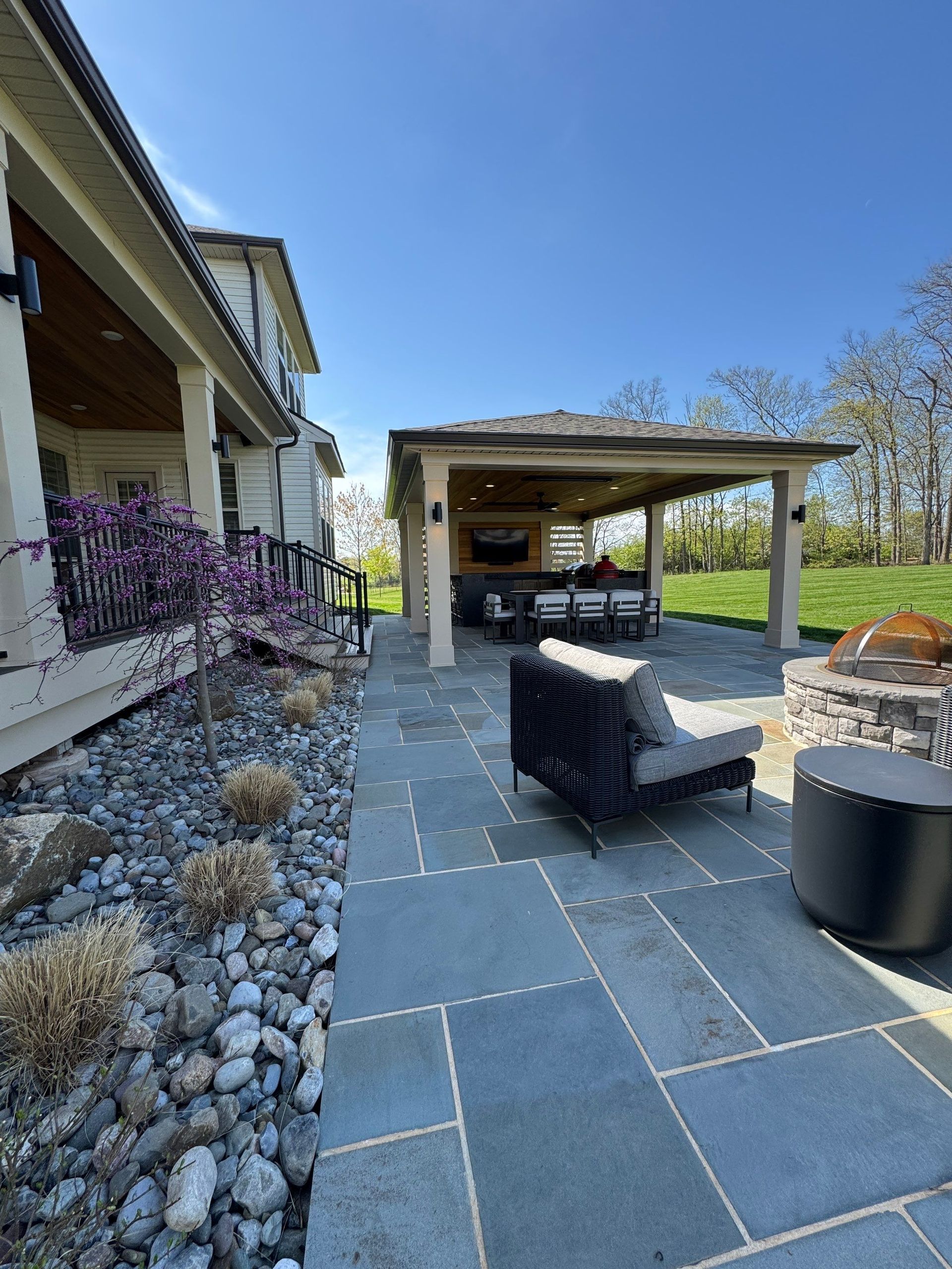 Patio with dark wicker seating, stone pavers, pergola, and house exterior under a blue sky