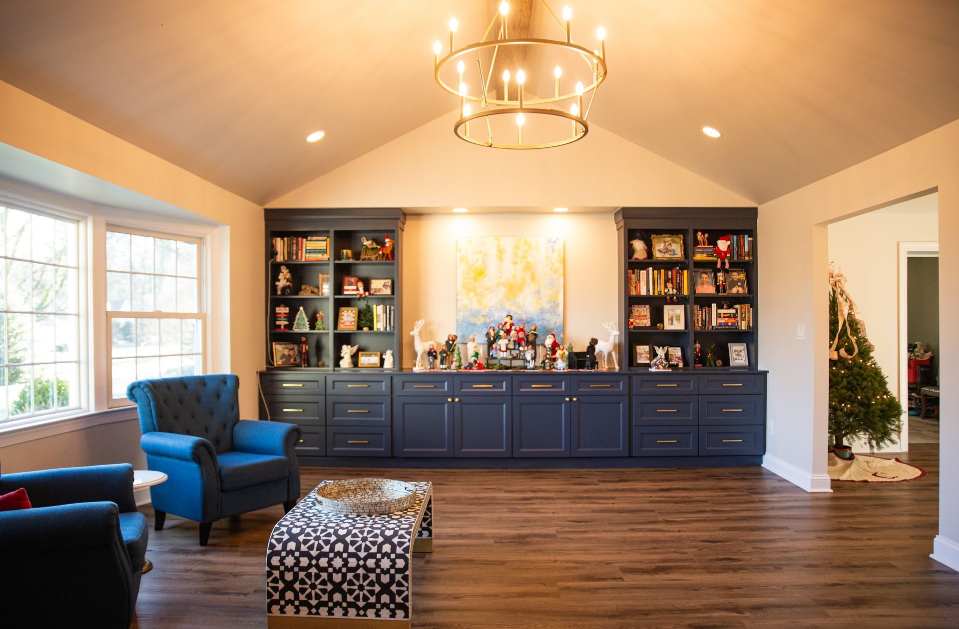 Bright living room with blue chairs, built-in shelves, large cabinet, chandelier, and Christmas tree
