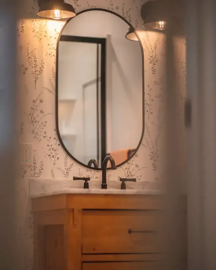 Bathroom vanity with oval mirror, black faucet, and warm wall sconces over a wooden cabinet