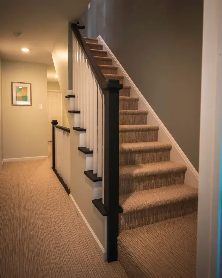 Carpeted staircase with black railing in a beige hallway, leading upstairs.