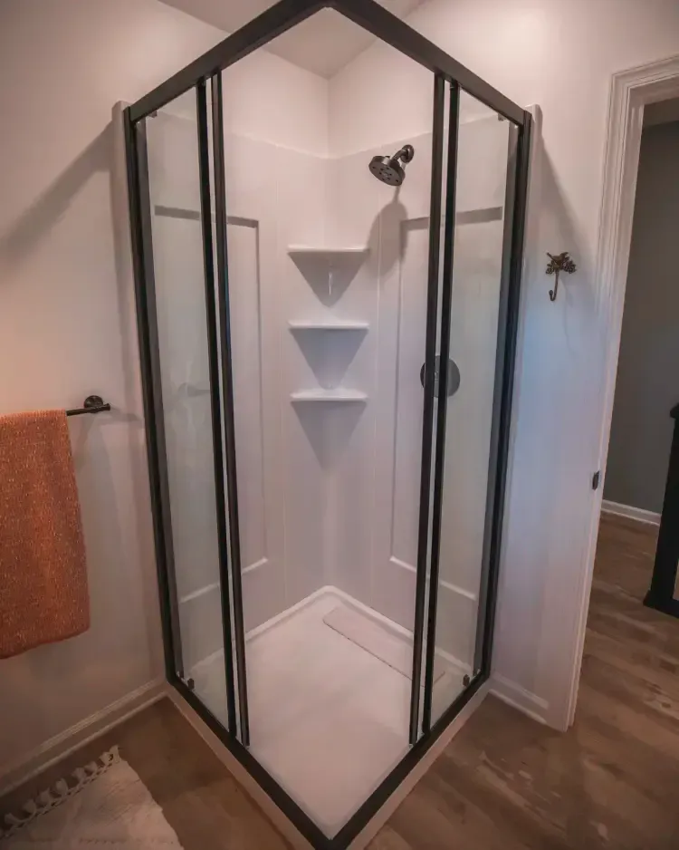 Glass-enclosed shower with black frame, white tile walls, and built-in corner shelves in a bathroom