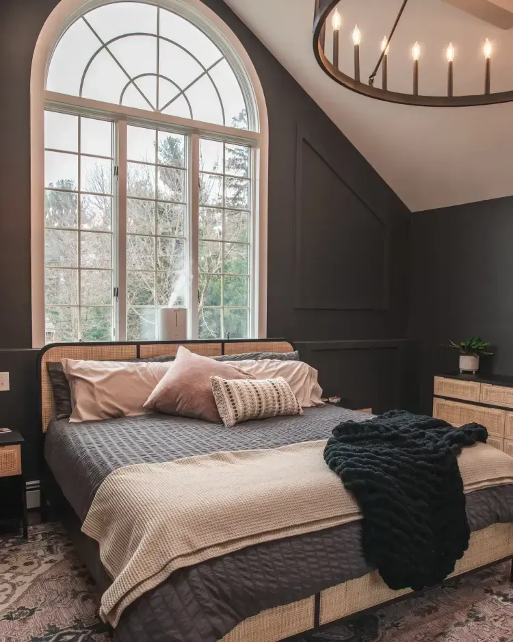 Dark cozy bedroom with arched window, black walls, and a neatly made bed with neutral bedding.