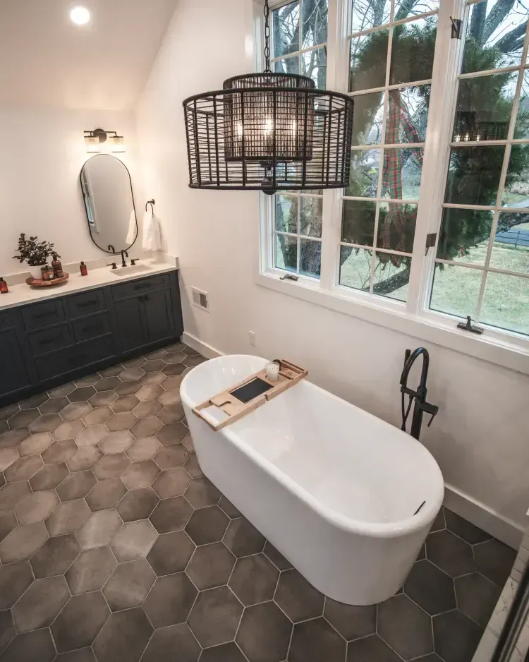 Bright modern bathroom with freestanding tub, hex tile floor, large windows, and woven pendant light