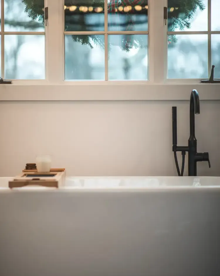 Minimalist bathroom with a white tub, black faucet, and candles by a window