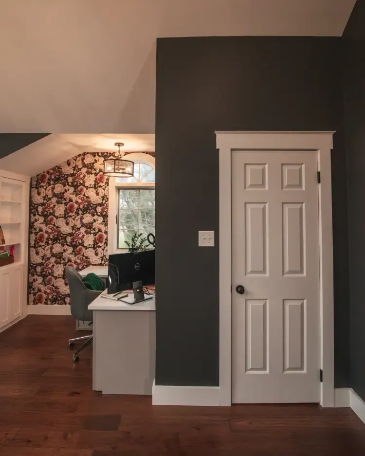 Home interior with dark accent wall, white door, desk, and floral wallpaper in the adjoining room