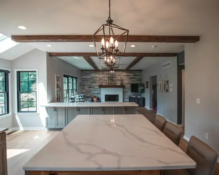 Modern open-concept kitchen and dining area with marble island, pendant lights, and stone fireplace beyond.