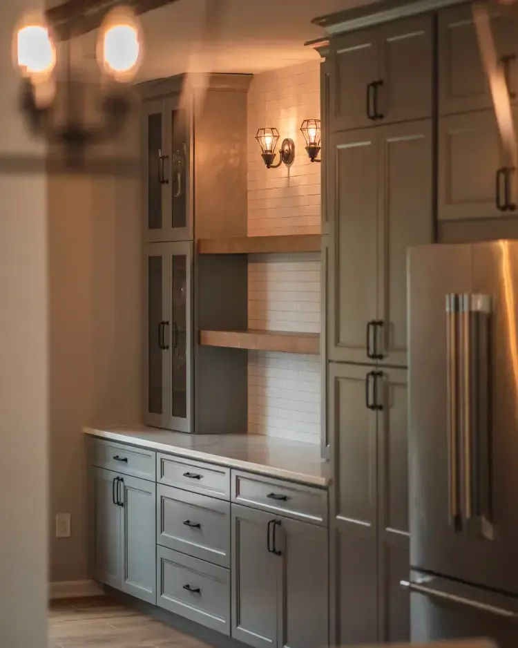 Built-in gray kitchen cabinets with a stainless steel refrigerator and warm wall sconces in a modern kitchen