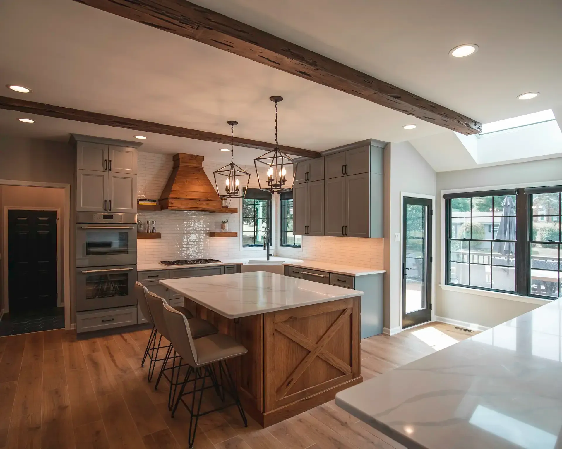 Modern kitchen with a large island, wood beams, pendant lights, and bright windows.
