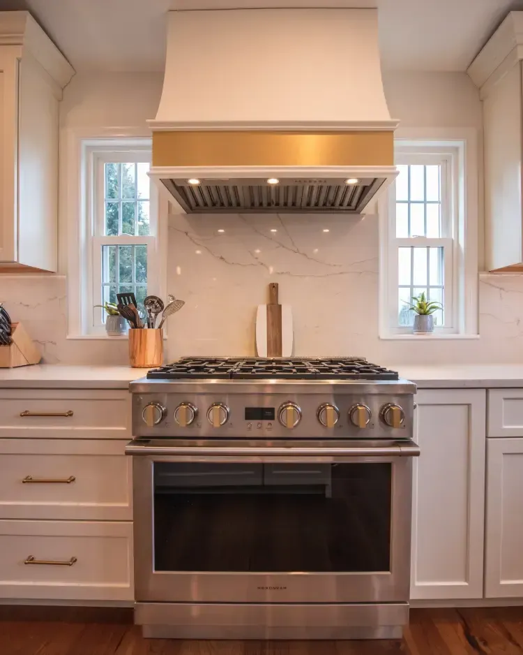 Modern kitchen with stainless steel range, white cabinets, and two narrow windows around a marble backsplash.