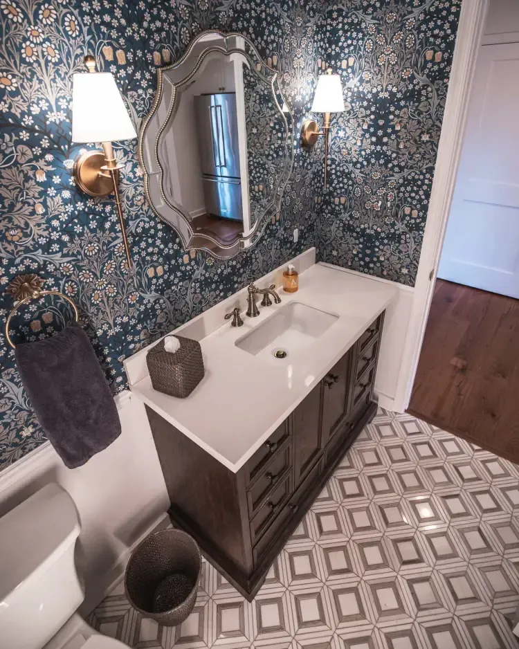 Elegant small bathroom with patterned wallpaper, white vanity, wall sconces, and ornate mirror.