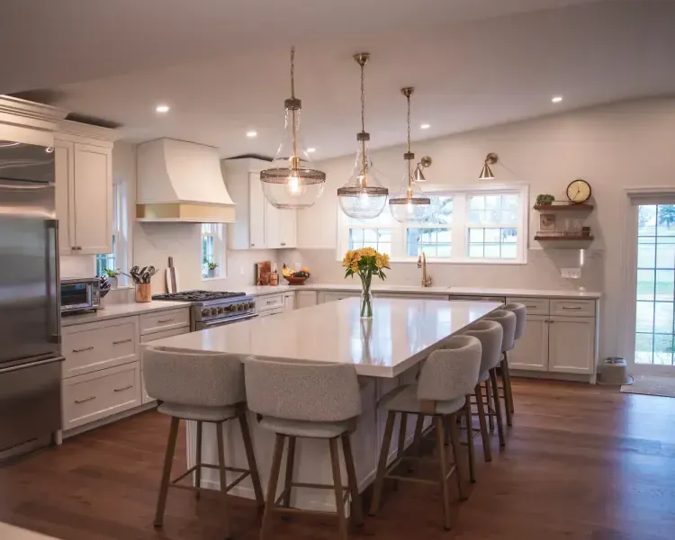 Bright modern kitchen with a large island, gray stools, pendant lights, and wood floors