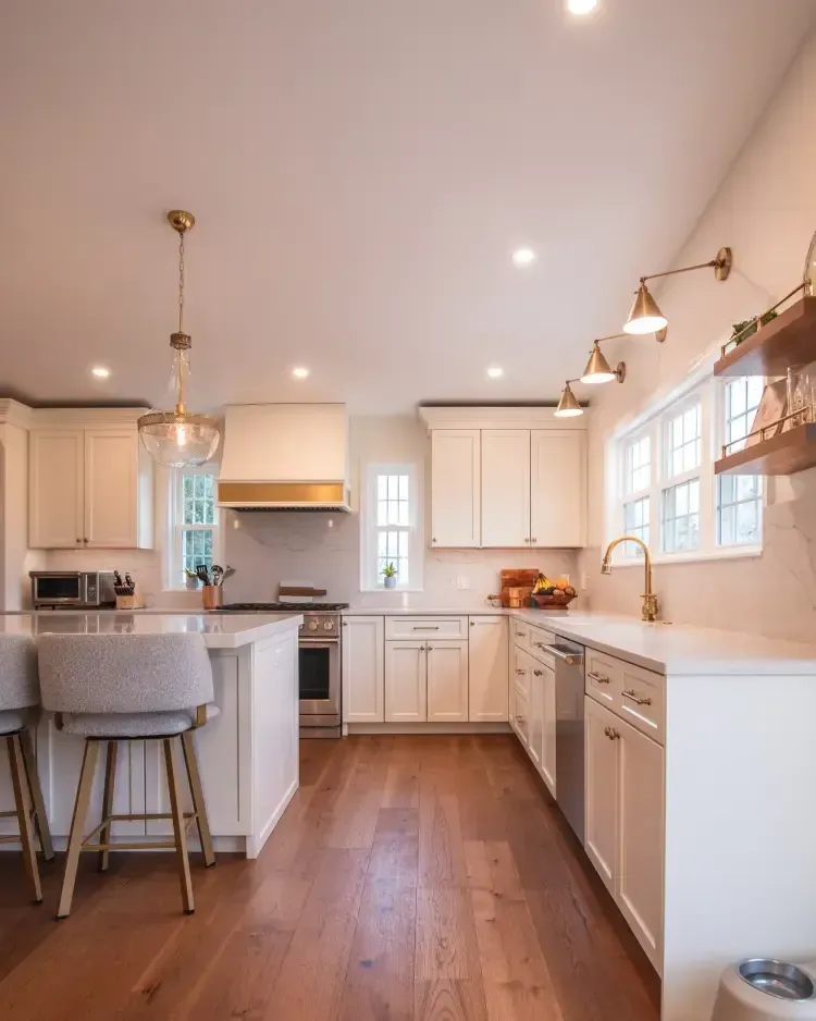 Bright modern kitchen with wood floors, white cabinets, island stools, and pendant lights.