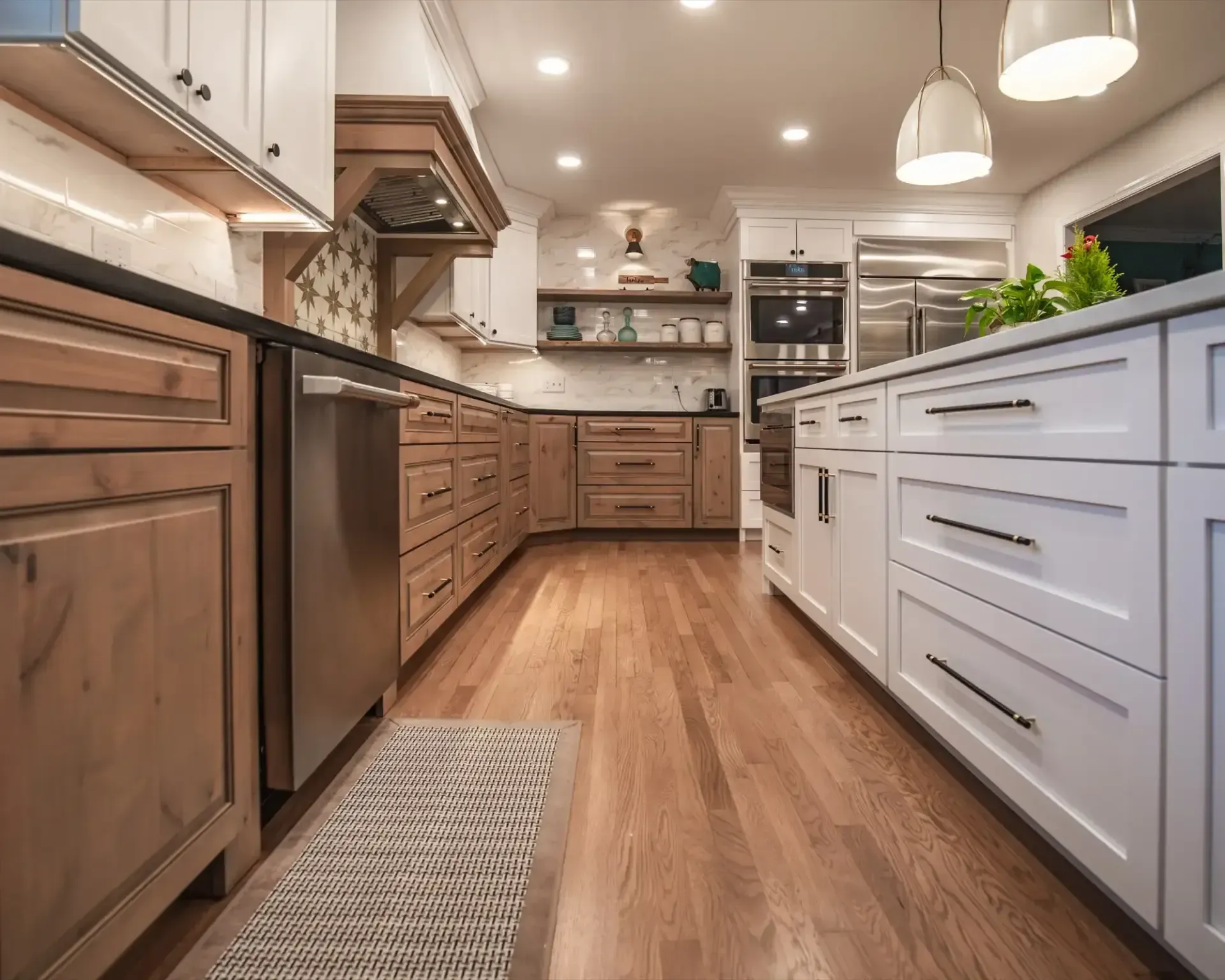 Modern kitchen with wood floors, white island, brown cabinets, pendant lights, and stainless appliances