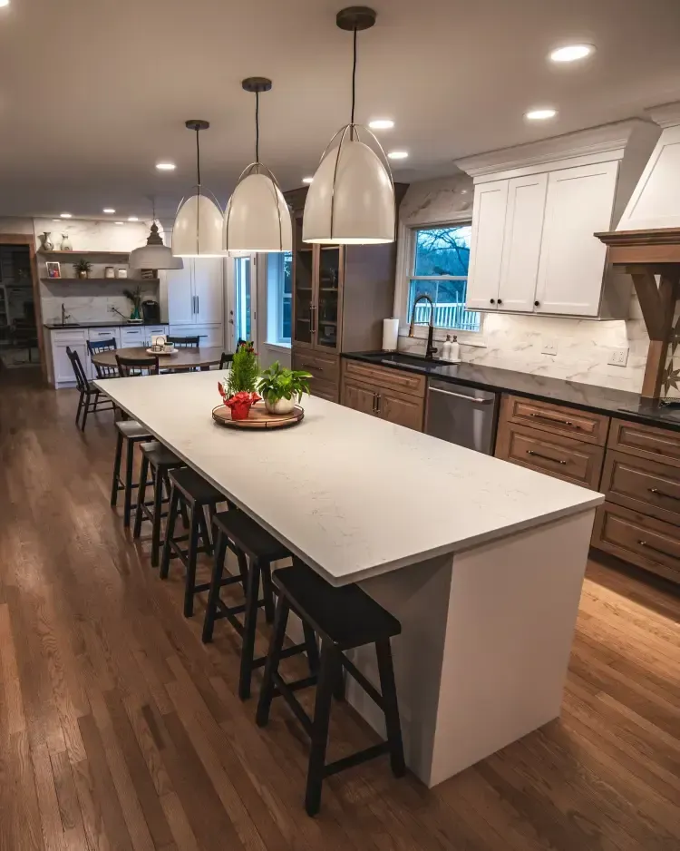 Modern kitchen with a large island, black stools, pendant lights, white cabinets, and wood floors.