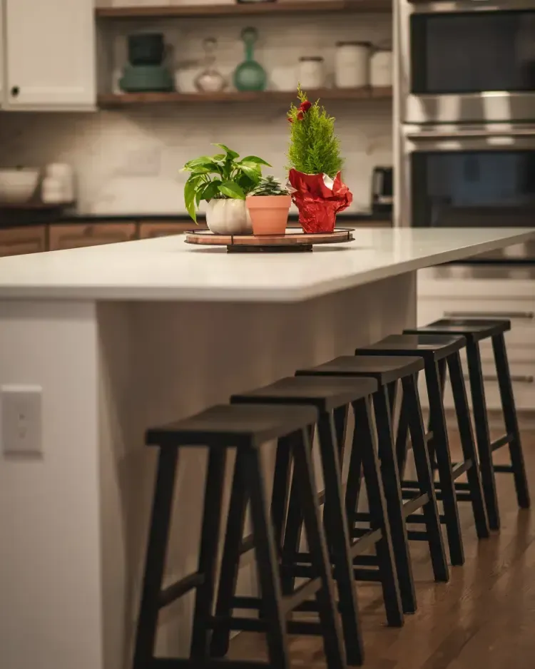 Modern kitchen with a white island, black stools, and potted herbs on a tray