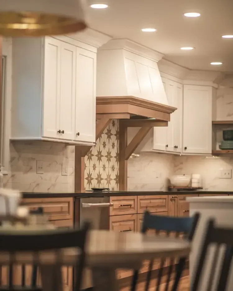 Modern kitchen with white cabinets, wood accents, patterned backsplash, and a blurred dining table in front