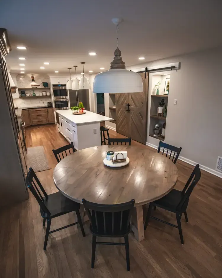 Dining area with round wooden table, black chairs, and a modern kitchen in the background.