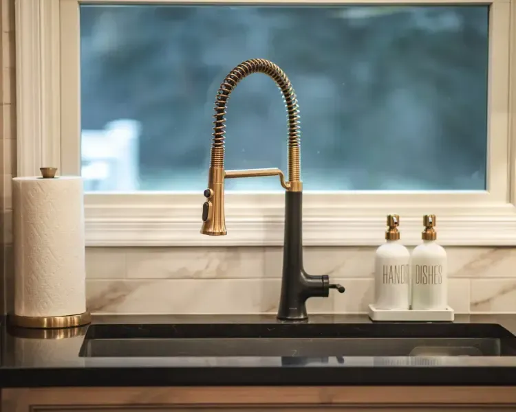 Modern kitchen sink with black faucet, brass spring sprayer, and soap dispensers by a window