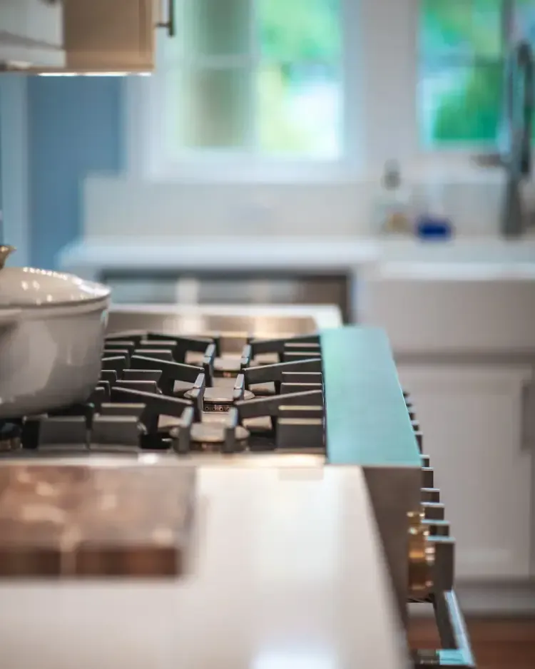 Kitchen stovetop with a pot on the burner, viewed from the side near a bright sink window.