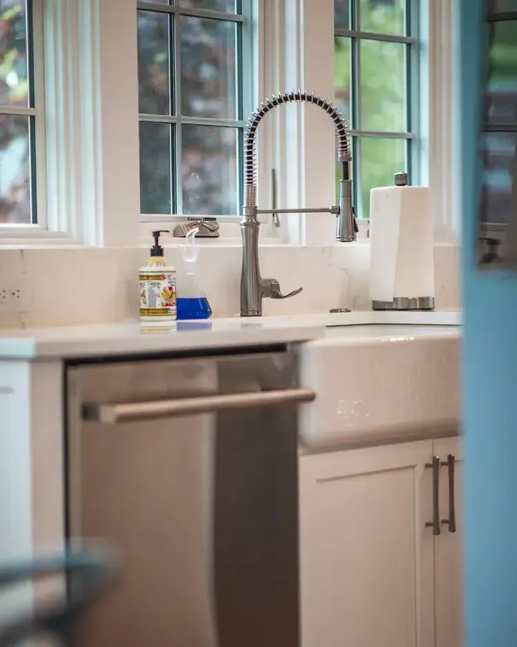 Modern kitchen sink with chrome faucet, white cabinets, and countertop items near a window.