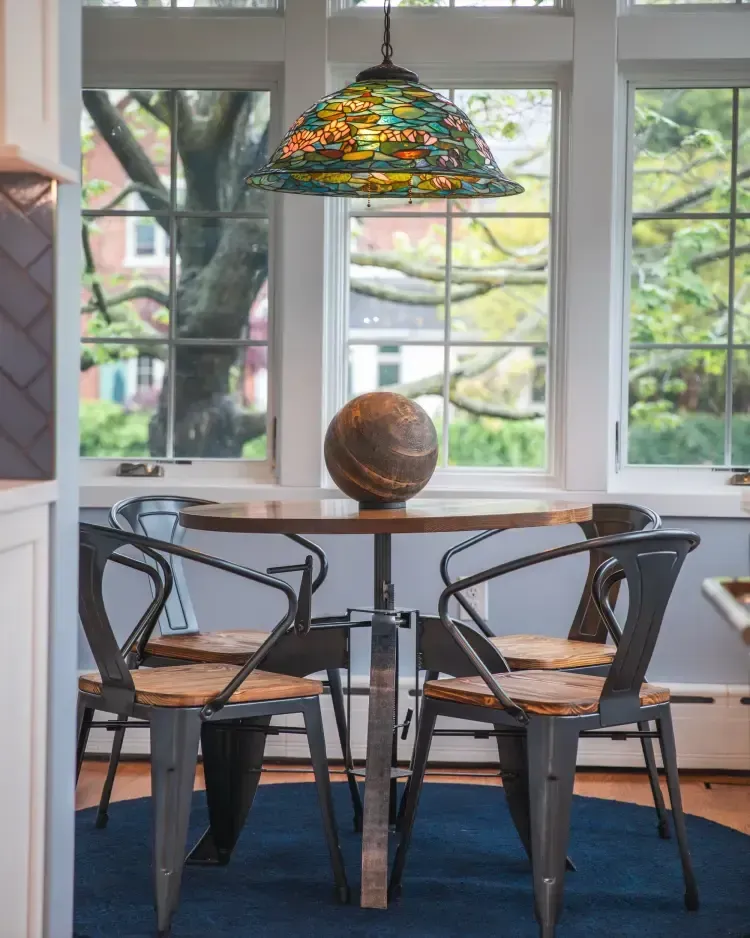 Dining nook with round table, two black chairs, stained-glass pendant, and large window view