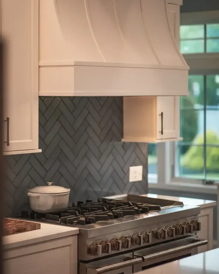 Modern kitchen with gray herringbone backsplash, stainless gas range, and white cabinets