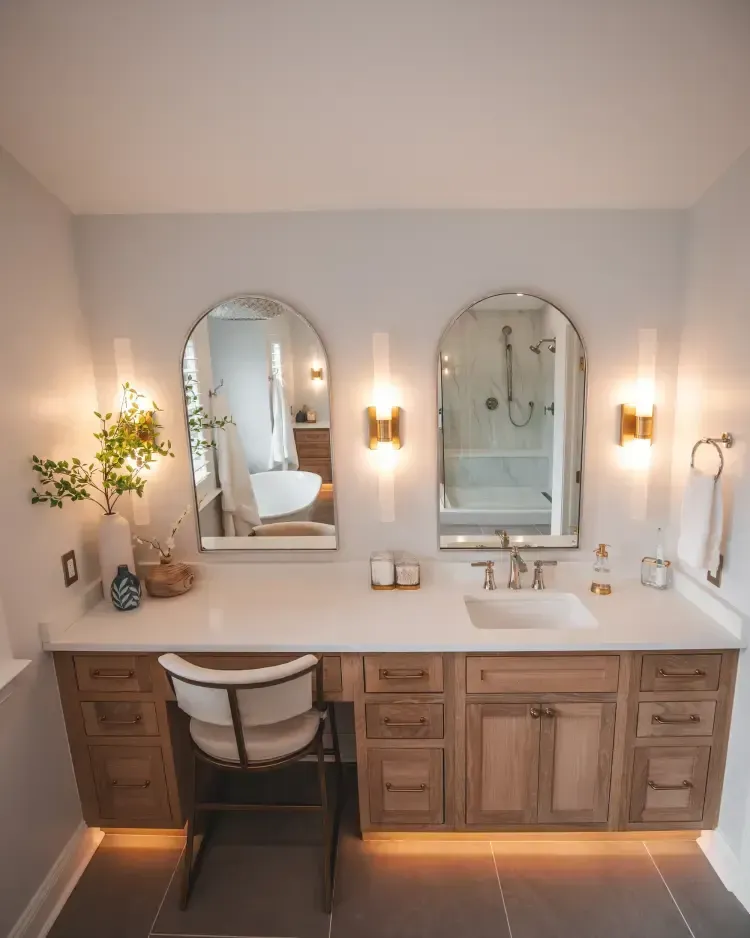 Modern bathroom vanity with dual mirrors, warm sconces, and wooden cabinets against light gray walls