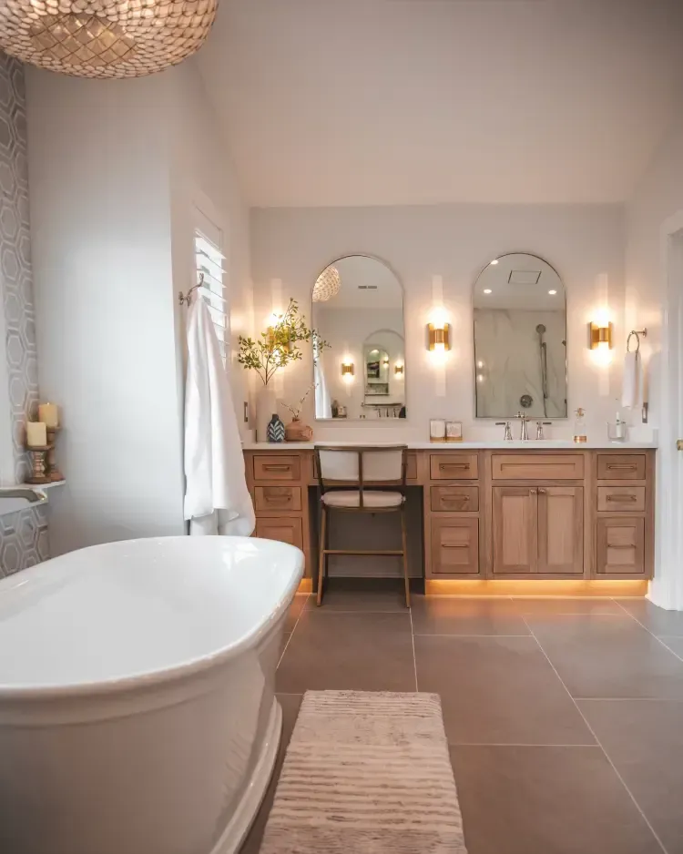Bright modern bathroom with freestanding tub, double vanity, arched mirrors, and warm lighting