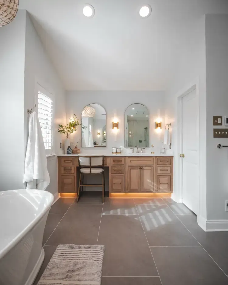 Bright bathroom with white tub, double vanity, wall sconces, and dark tile floor.