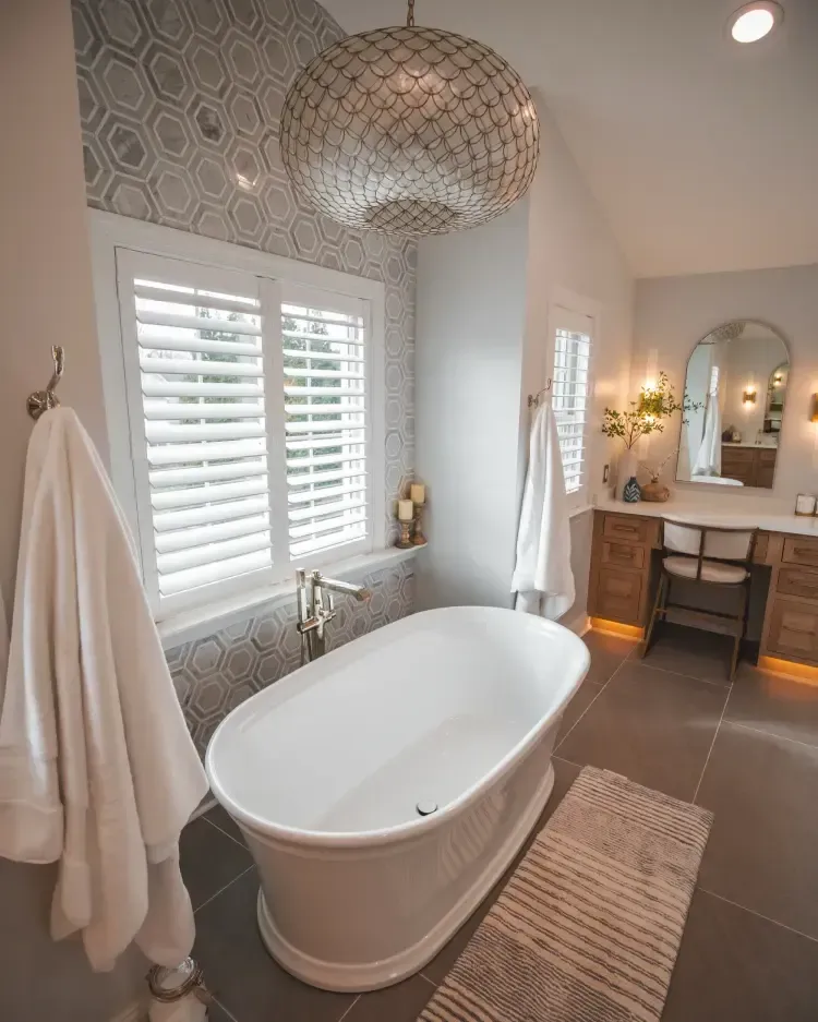 Bright modern bathroom with a freestanding tub, window shutters, patterned tile, and vanity mirror