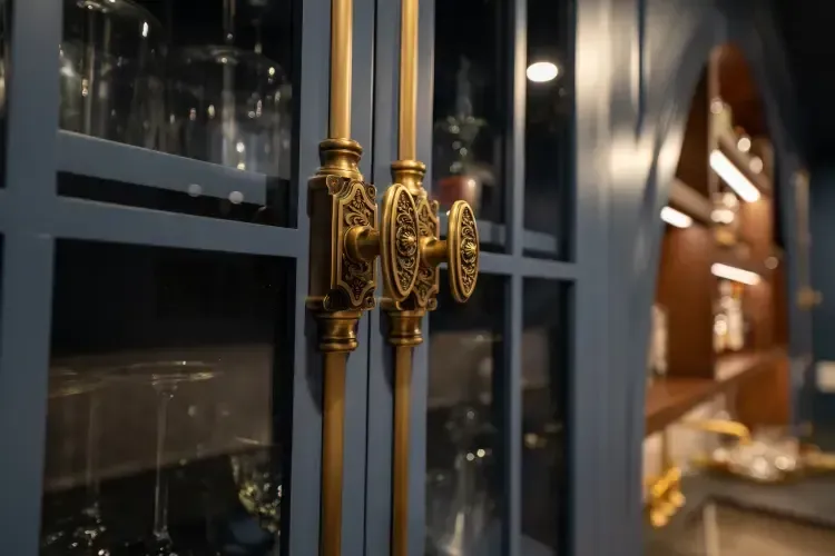 Ornate gold door handles on dark glass doors, with a softly lit interior hallway in the background