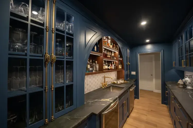 Blue kitchen with glass-front cabinets, dark counters, and wood floors under warm lighting