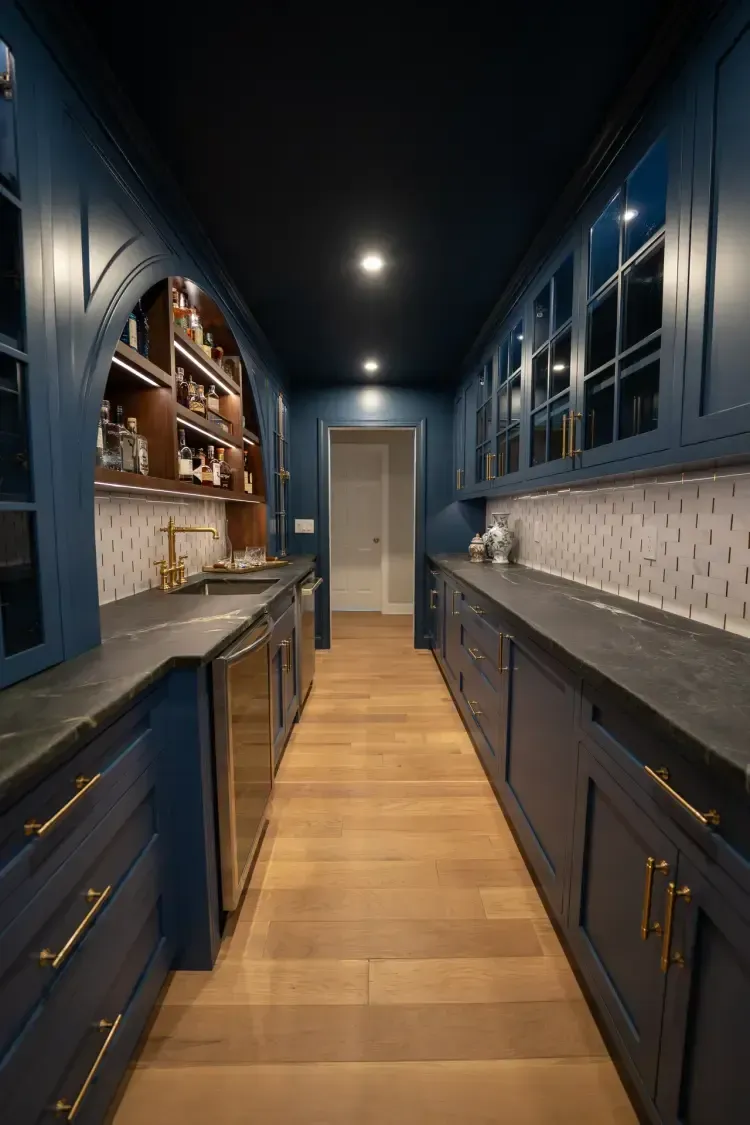 Narrow blue kitchen with wood floor, dark counters, and overhead lights stretching to a door at the end.