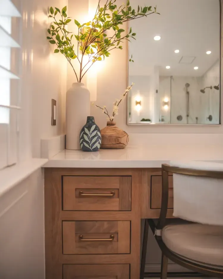 Bright bathroom vanity with wood drawers, lit mirror, and decorative vases on a white countertop