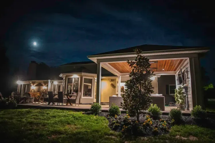 Modern house with lit porch and patio at night under a moonlit sky