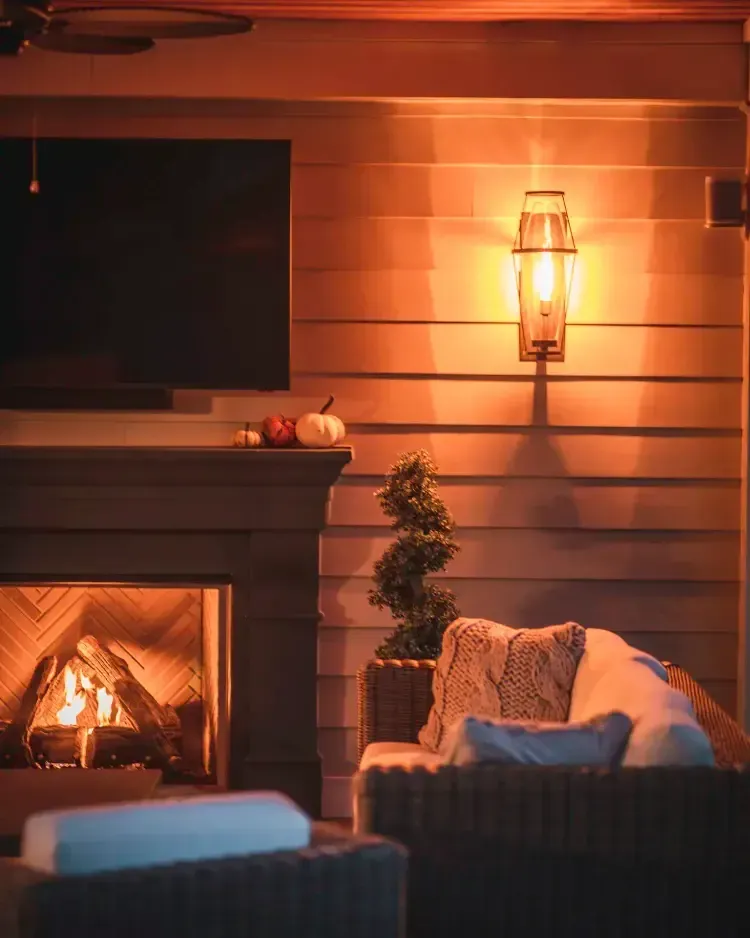 Cozy living room with a lit fireplace, wall sconce, and armchair in warm amber light