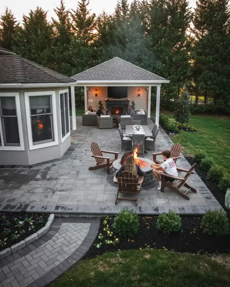 Backyard patio with a fire pit, outdoor chairs, and a covered seating area at dusk