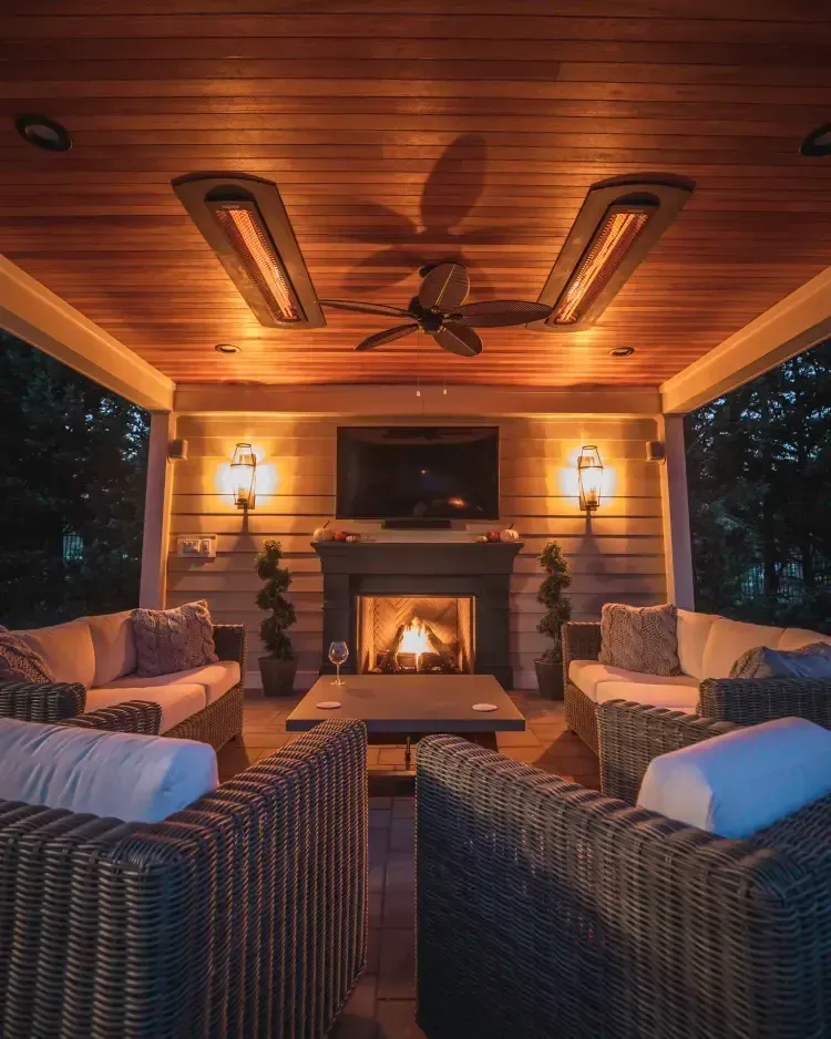 Cozy covered porch with wicker chairs, fireplace, wall sconces, and ceiling fans at dusk