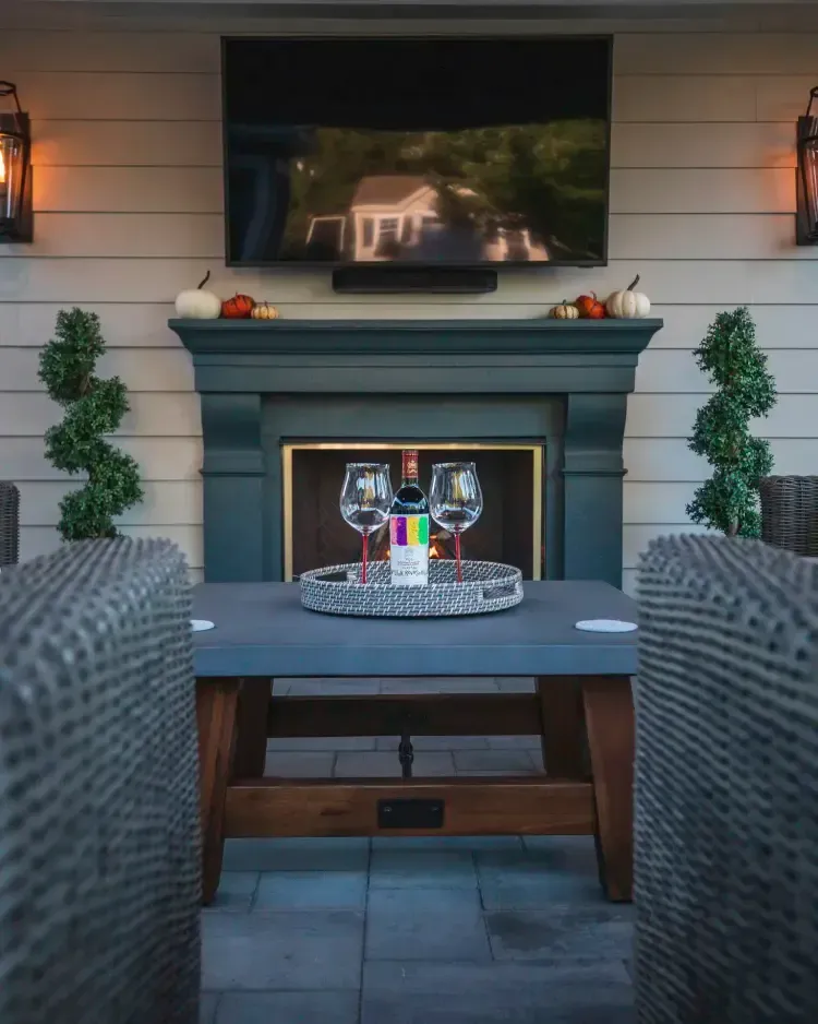 Outdoor patio with fireplace, TV, and a table set for drinks between two wicker sofas.
