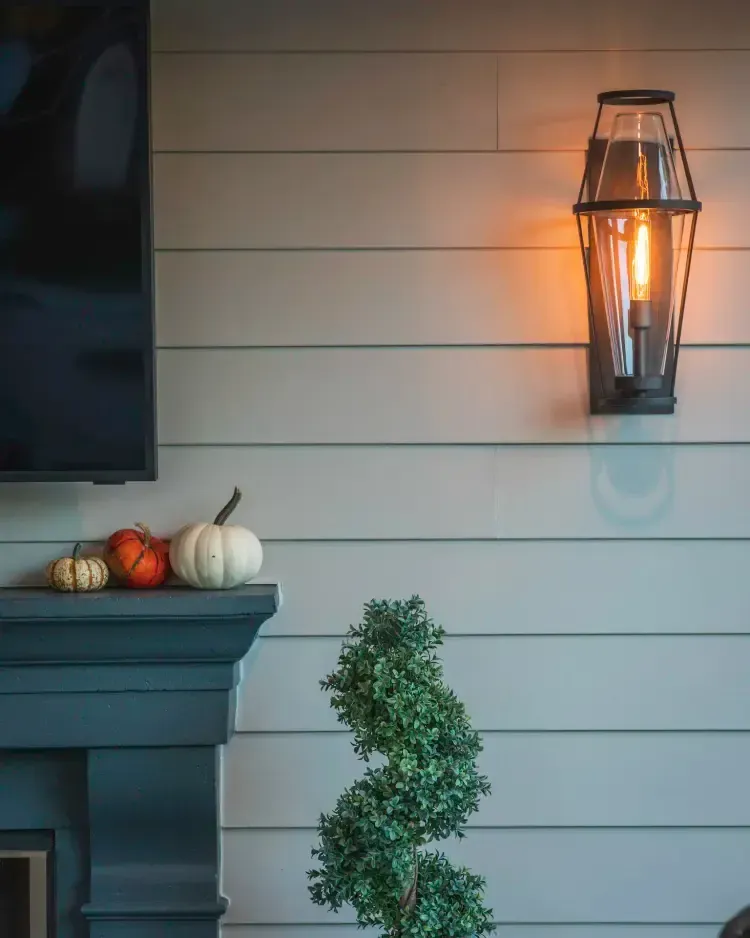 Porch wall with lit lantern, pumpkins on mantel, and greenery