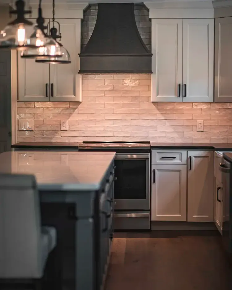 Modern kitchen with white cabinets, dark range hood, subway tile backsplash, and island lighting