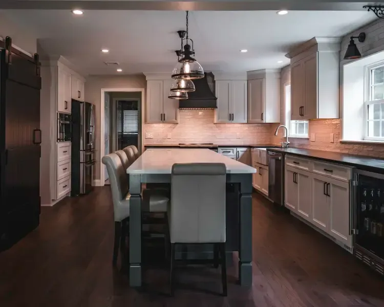 Modern kitchen with central island, dark wood floors, white cabinets, and pendant lights